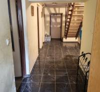 Interiér rodinného domu s tmavou dlažbou a dřevěným schodištěm.