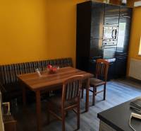 Jídelna v rodinném domě s dřevěným stolem, židlemi a podlahou s dřevěným dekorem.