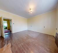 Pokoj s podlahou s dřevěným dekorem, světlými stěnami a oknem s bílou záclonou.