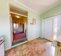 Chodba s koberci a stolem v rodinném domě, zelené stěny, velké skleněné dveře.