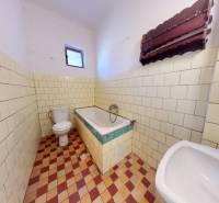 Koupelna v rodinném domě s vanou, umyvadlem a toaletou, obložená dlaždičkami.