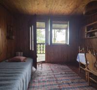 Interiér chaty s dřevěným dekorem, postel, stůl, židle a kobereček.