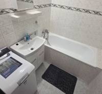 Koupelna s vanou a pračkou v 1-pokojovém bytě, světlé obklady a úložný prostor.