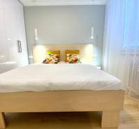 Světlá ložnice v dvoupokojovém bytě s barevnými polštáři na posteli.