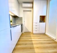 Kuchyně s bílými skříňkami a podlahou s dřevěným dekorem v 2-pokojovém bytě.