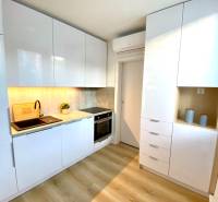 Kuchyně v 2-pokojovém bytě s bílými skříňkami a podlahou s dřevěným dekorem.