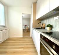 Kuchyně v 2pokojovém bytě s bílými skříňkami a podlahou s dřevěným dekorem.