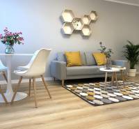 Obývací pokoj dvoupokojového bytu s podlahou s dřevěným dekorem, šedou sedačkou a dekorativními hexagony.