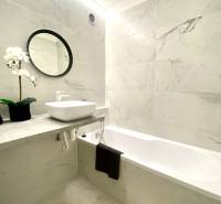 Koupelna v 2-pokojovém bytě s vanou, zrcadlem a květinovou dekorací.