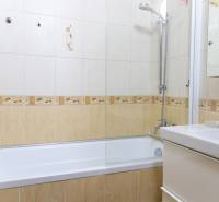 Koupelna s obkladem a vanou ve 4-pokojovém bytě, světlé barvy a sprchová růžice.
