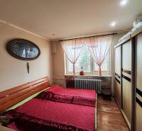 Ložnice ve 4pokojovém bytě s postelí, skříní a podlahou s dřevěným dekorem.