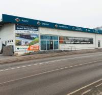 Obchodní prostory na Kamennej ulici v Žilině s reklamními nápisy a prázdným parkovištěm.