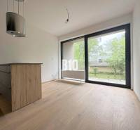 Interiér 2-pokojového bytu s dřevěnou podlahou a velkým oknem na zelený exteriér.