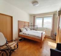 Pokoj ve 3-pokojovém bytě s postelí, stolem, podlahou s dřevěným dekorem a žlutými stěnami.