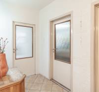 Chodba ve 3-pokojovém bytě s květinou na dřevěném stolku a dveřmi se sklem.