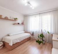 Světlý pokoj s postelí, psacím stolem a podlahou s dřevěným dekorem ve 3pokojovém bytě.