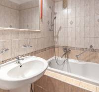 Koupelna v 3-pokojovém bytě s vanou, obklady a umyvadlem, doplněná zrcadlem.
