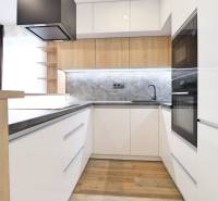 Kuchyně v 3-pokojovém bytě s bílými skříňkami a podlahou s dřevěným dekorem.