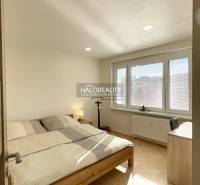 Ložnice v jednopokojovém bytě s podlahou s dřevěným dekorem a velkými okny.