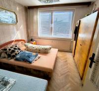 Ložnice ve 3pokojovém bytě s postelí, skříňkou a podlahou s dřevěným dekorem.