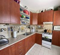 Kuchyně v 2-pokojovém bytě s dřevěnými skříňkami a bílou dlažbou.