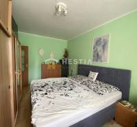 Ložnice v 2pokojovém bytě s postelí a nábytkem, stěny jsou světle zelené.