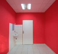 Interiér obchodních prostor, červené stěny, bílé dveře a umyvadlo, keramická dlažba.