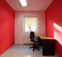 Kancelář s červenými stěnami, černou židlí a stolem, světlý interiér.