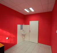 Interiér obchodního prostoru s červenými stěnami, umyvadlem a bílými dlaždicemi.