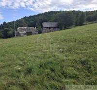 Travnatý svah s budovami v pozadí, obklopený přírodou v Horním Tisovníku, ideální na Pozemky - bydlení.