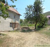 Rodinný dům v Šiatorské Bukovince se zahradou a stromy pod modrou oblohou.