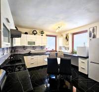 Kuchyně v rodinném domě s černým lesklým obkladem a bílým nábytkem.