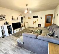 Obývací pokoj v rodinném domě s podlahou s dřevěným dekorem, šedou sedačkou a moderním osvětlením.