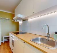 Kuchyně v 1-pokojovém bytě s bílými skříňkami a podlahou s dřevěným dekorem.