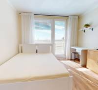 Pokoj s postelí, psacím stolem a úložným prostorem v 1-pokojovém bytě.