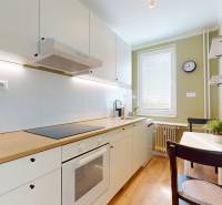 Kuchyně v 1-pokojovém bytě s bílými skříňkami a podlahou s dřevěným dekorem.