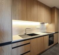 Kuchyně s dřevěným dekorem, černými detaily, vestavěnými spotřebiči ve 3-pokojovém bytě.