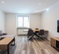 Obývací pokoj s podlahou s dřevěným dekorem, sedačkou, jídelním stolem a televizí ve 3-pokojovém bytě.