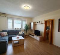 Světlý obývací pokoj s modrou sedačkou v 3-pokojovém bytě, podlaha s dřevěným dekorem.