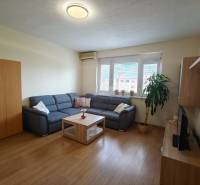 Obývací pokoj s rohovou sedačkou, podlahou s dřevěným dekorem a TV ve 3-pokojovém bytě.