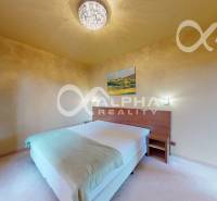 Světlá ložnice v 2-pokojovém bytě s obrazem na stěně a pohodlnou postelí.