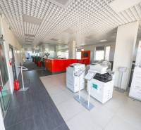 Interiér kanceláře s tiskárnami, červeným recepčním pultem a vysokým stropem.