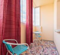 Balkon v 1-pokojovém bytě s červenými závěsy, stolkem a rostlinou na parapetu.