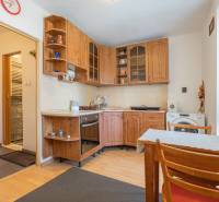 Kuchyně s rohovou linkou v 1-pokojovém bytě, podlaha s dřevěným dekorem, jídelní stůl.