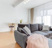 Světlý obývací pokoj s podlahou s dřevěným dekorem, pohodlnou sedačkou a jídelním koutem.