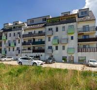 Budova s byty na ulici Vincenta Šikulu ve Stupavě obklopená auty a zelení.