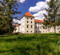 Historická budova obklopená zelení a stromy za slunečného dne.