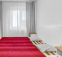 Ložnice v 2-pokojovém bytě s lůžkem s šedými polštáři, dekou a nočním stolkem.