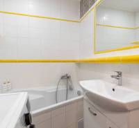 Koupelna rekreačního apartmánu s vanou, umyvadlem, pračkou a bílými obklady.