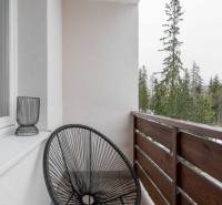 Balkon rekreačního apartmánu v Popradu s černým křeslem a výhledem na stromy.